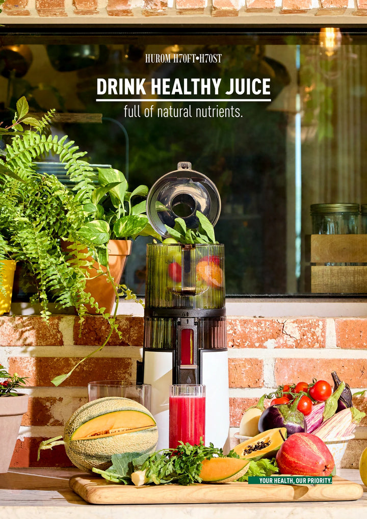 Black and white Hurom H410 slow juicer with ingredients and a glass of juice on a wooden surface, with text promoting healthy juice.