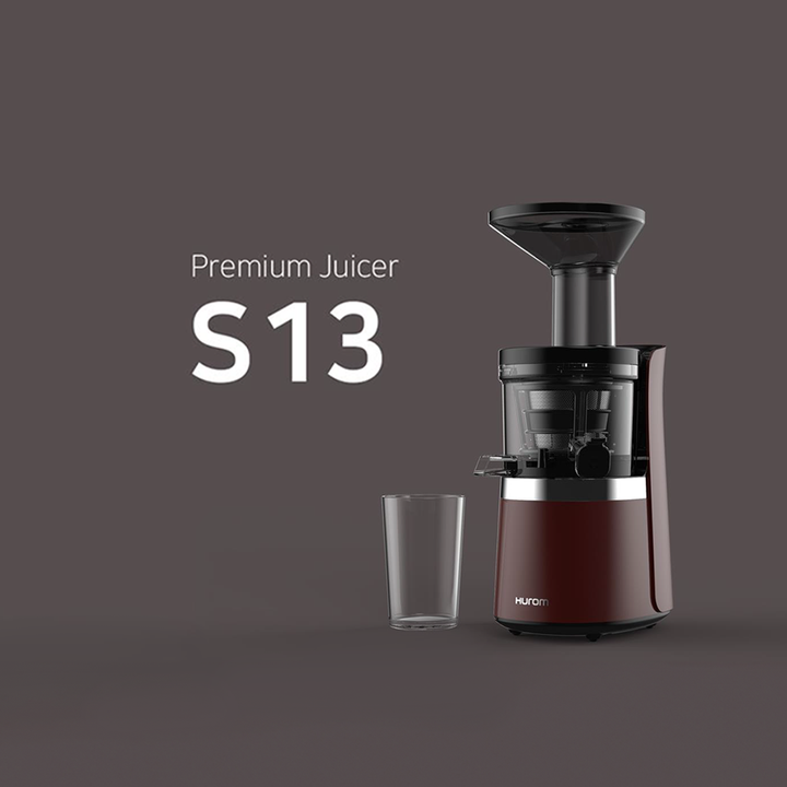 A red Hurom S13 slow juicer and a glass on a brown background