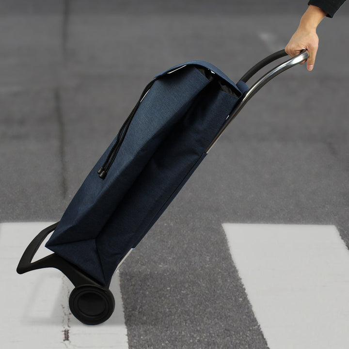 A blue Rolser Baby Joy Market & Shopping Trolley with an aluminum frame and a water-resistant polyester bag, being pulled by a hand.