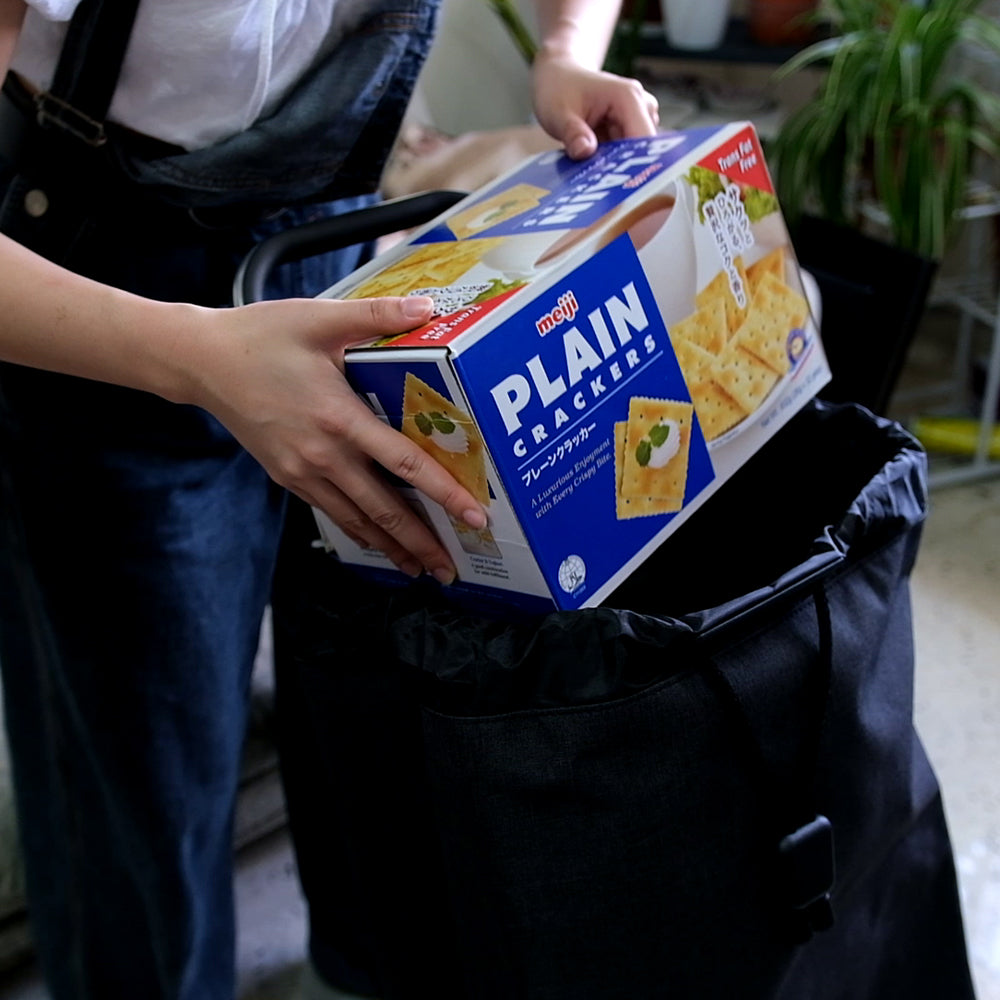 A navy blue Rolser Tweed shopping trolley with a carton of crackers being fitted in.