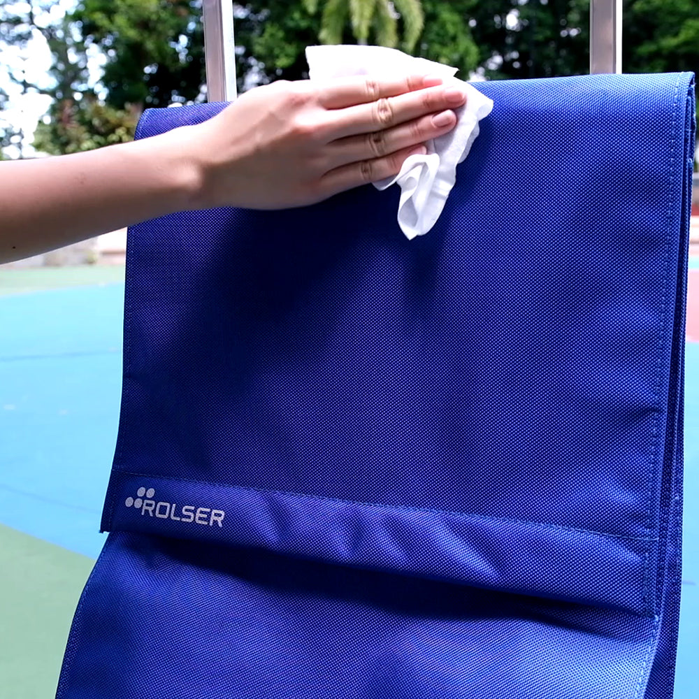 A blue foldable Rolser Plegamatic shopping trolley being wiped dry with a tissue paper.