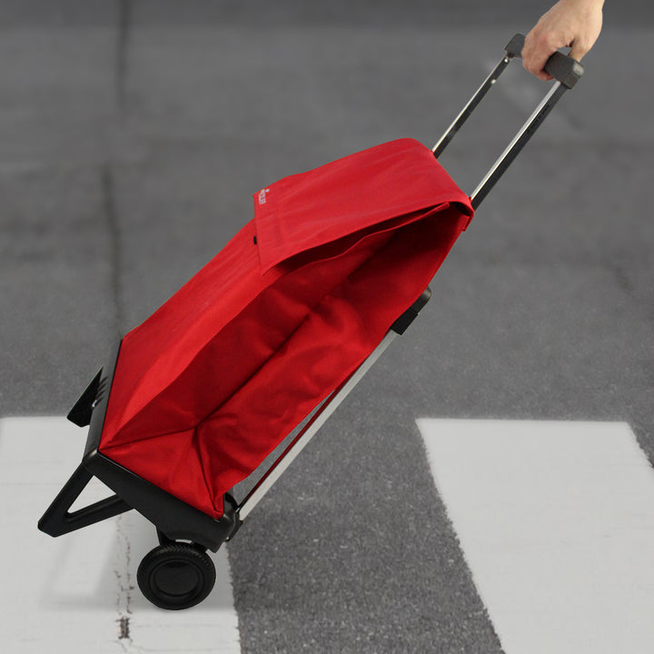 A red folded Rolser Plegamatic shopping trolley being pulled.